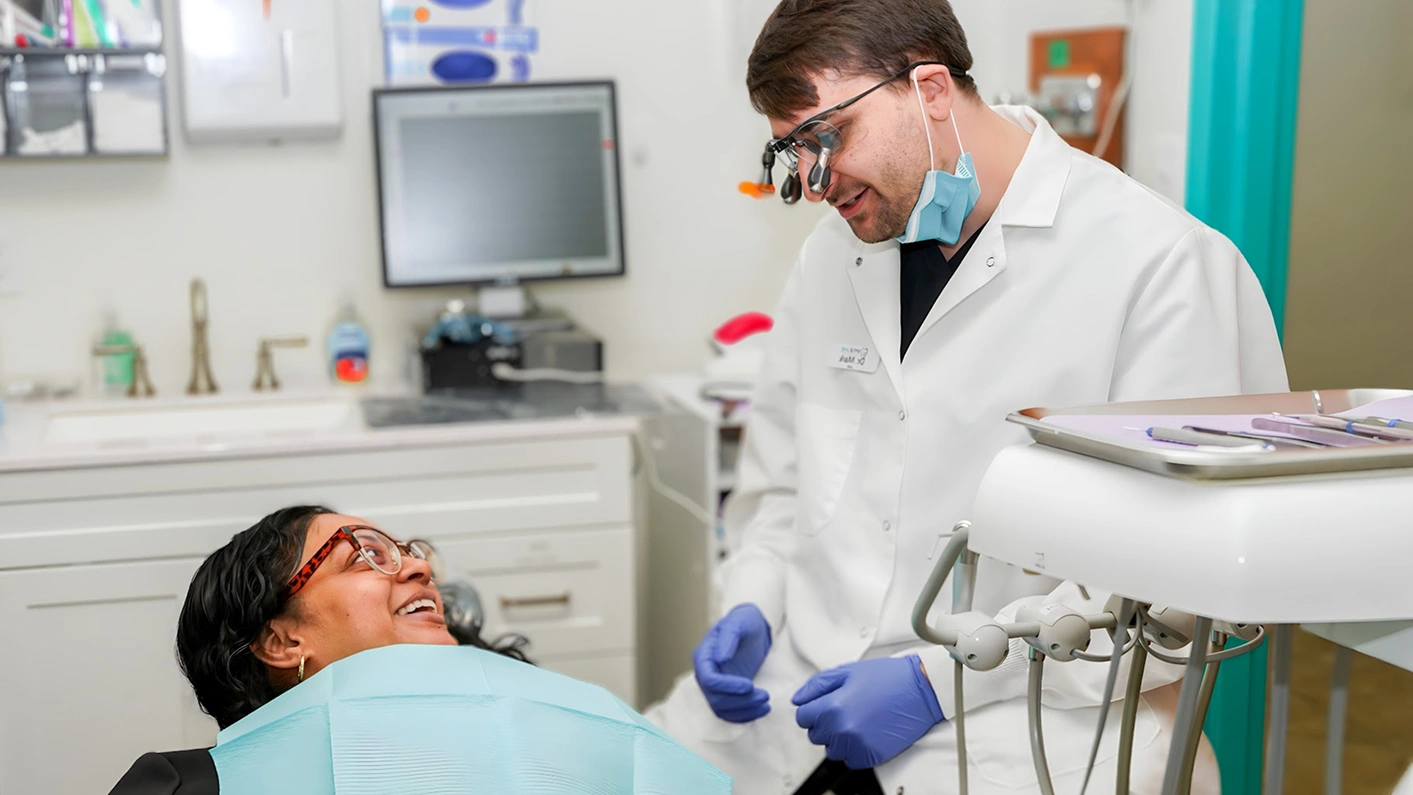 Dentist in blue gloves smiling with patient in dental chair during treatment at Fitchburg practice.