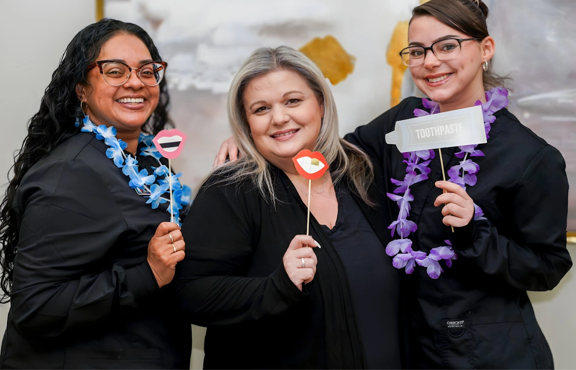 Three dental professionals in business attire holding festive props and leis celebrate accepting patient insurance.