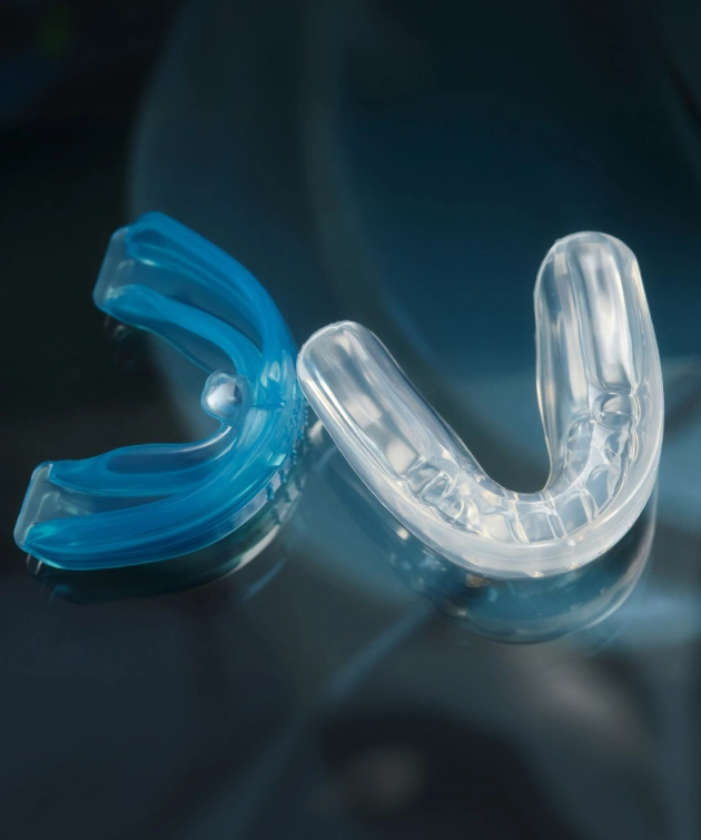 Blue and clear custom athletic mouthguards displayed on dark background.