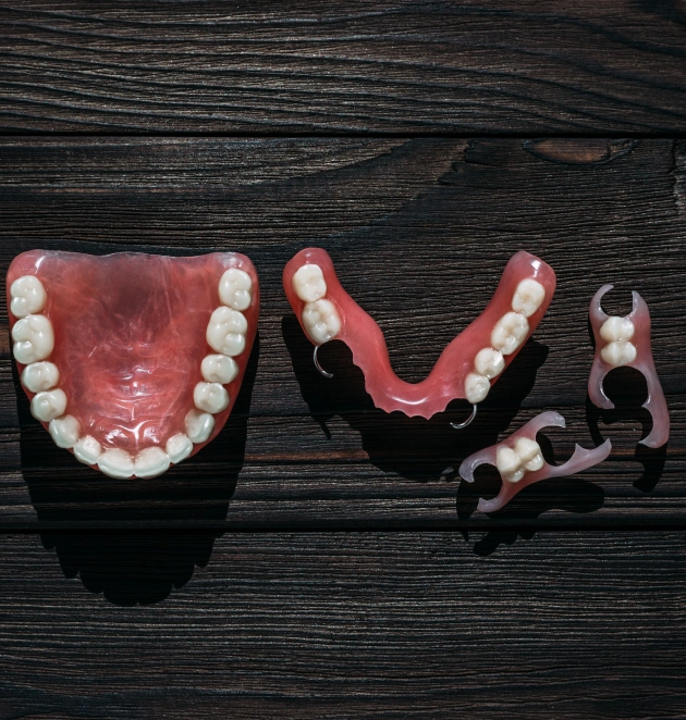 Three dental prosthetic models displaying complete and partial dentures with artificial teeth on dark wood background.