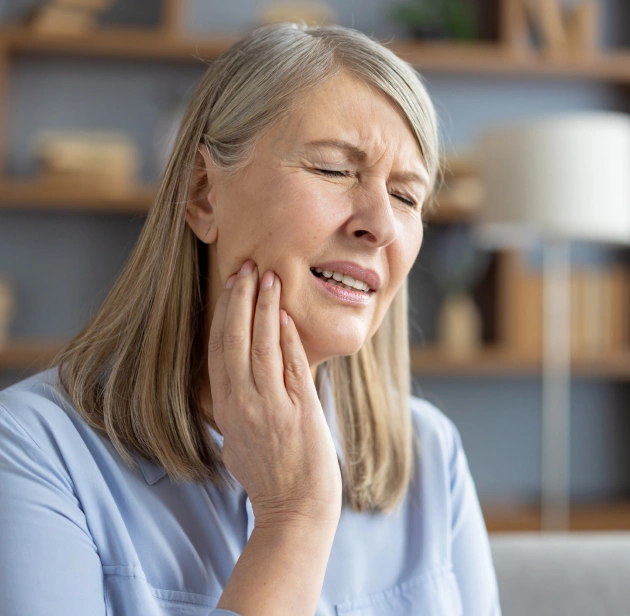 Woman holding her cheek in pain, indicating dental discomfort or emergency dental needs.