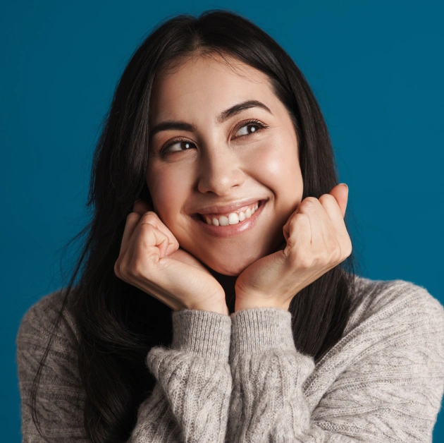 Smiling woman with healthy teeth in gray sweater against blue background.