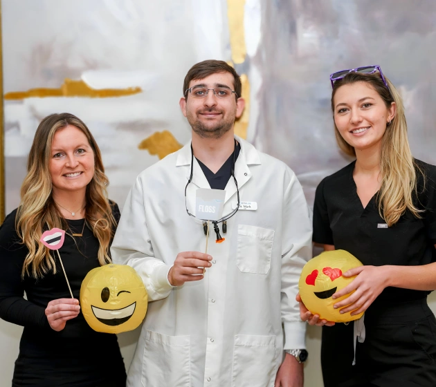 Three dental team members holding emoji stress balls, smiling at Fitchburg dental practice.