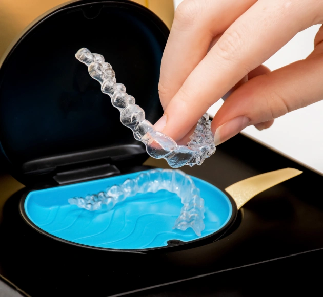 Clear Invisalign aligner being held over blue storage case showing proper fit and care.