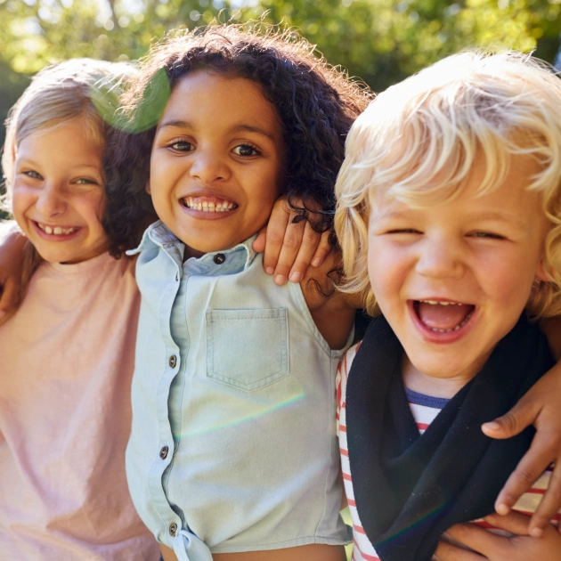 Three happy children smiling together outdoors in bright sunlight.