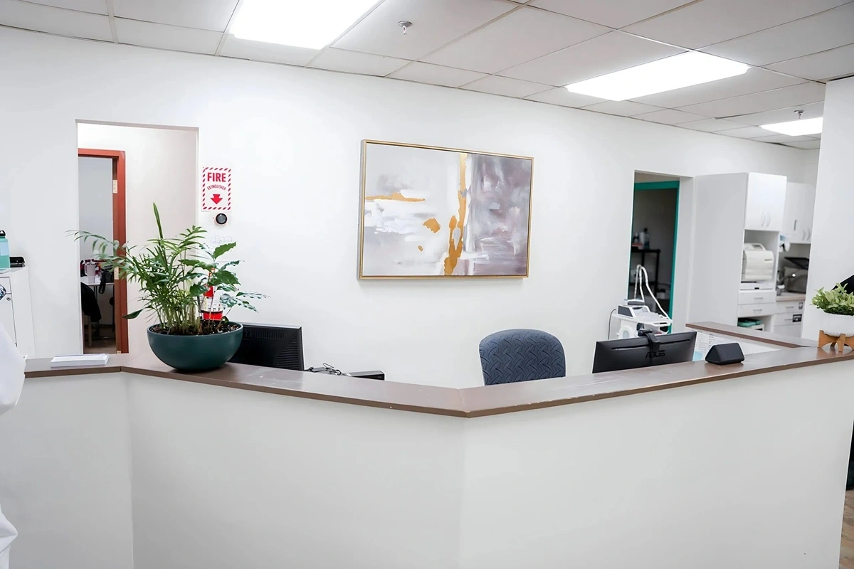 Modern dental office reception desk with white countertop, teal chair, potted plant, and framed abstract artwork.