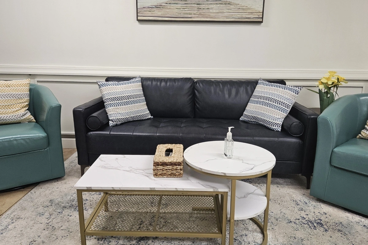 Modern dental office waiting room with black leather sofa, teal chairs, and marble coffee tables.