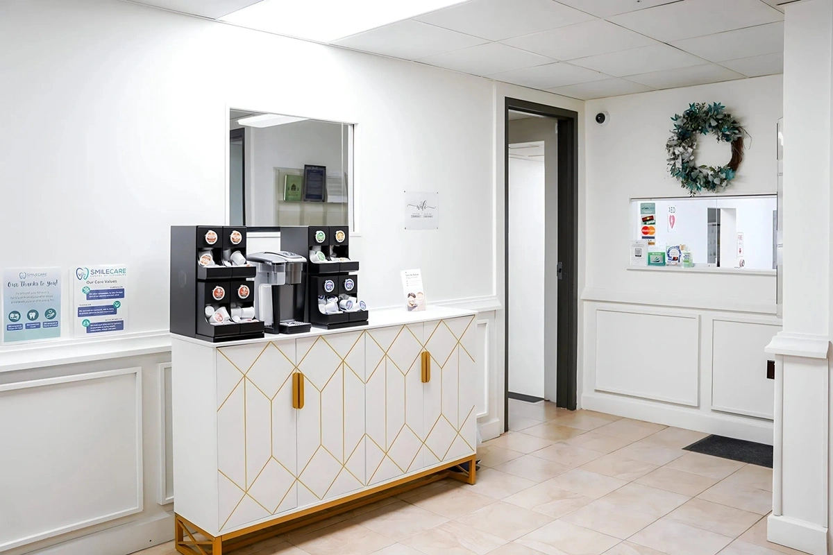 Modern dental office refreshment station with white cabinetry, geometric gold accents, and coffee service amenities.