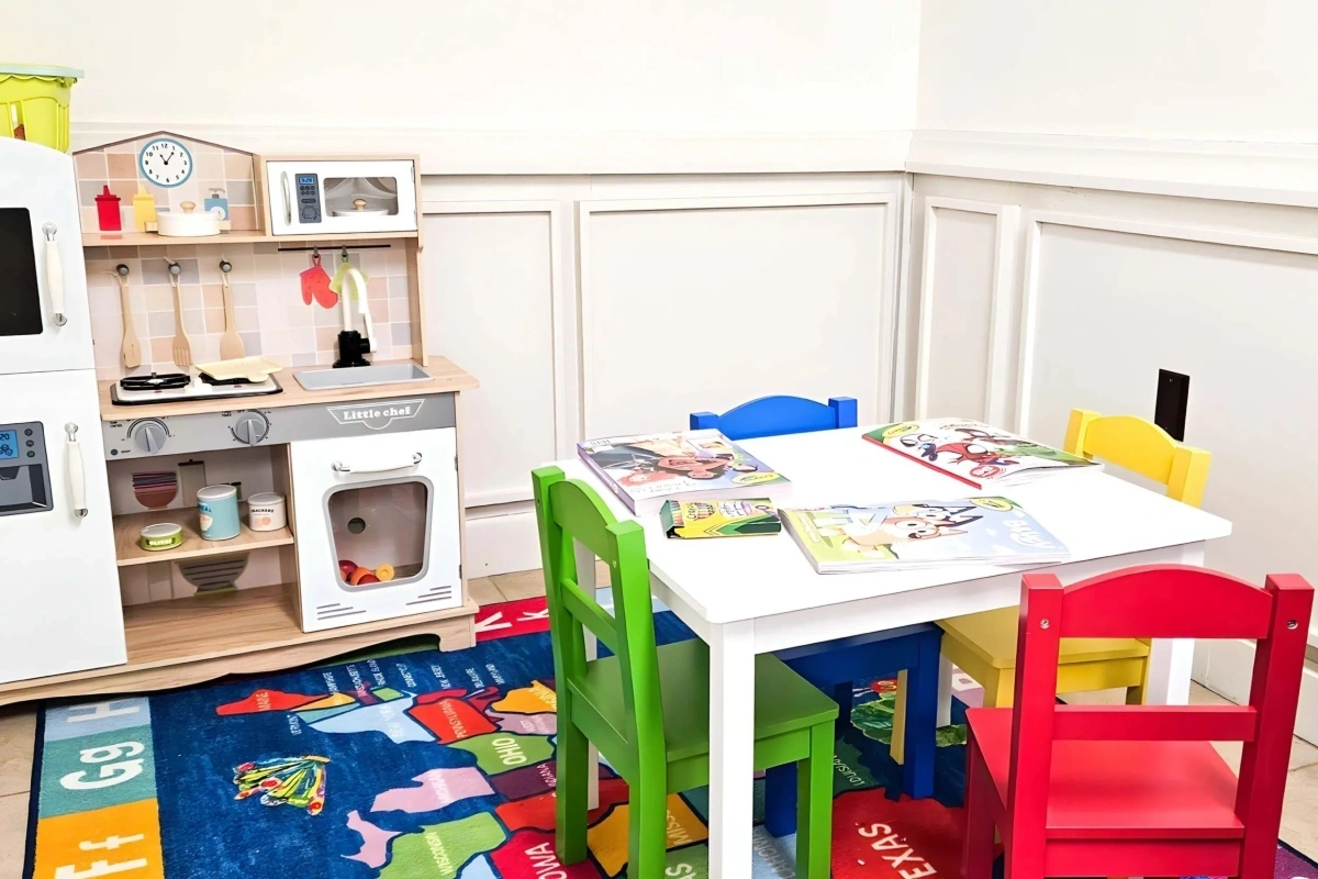 Kids play area at Fitchburg dental office featuring colorful table, chairs, play kitchen, educational books, and activity ru.