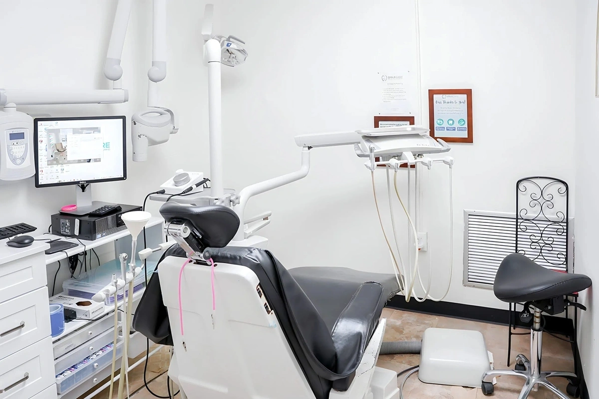 Modern dental treatment room with black patient chair, white overhead lighting, digital display, and sterilized instruments.