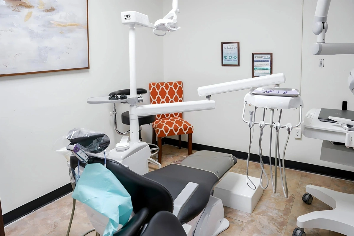 Modern dental operatory with treatment chair, overhead light, instruments, and waiting seating at Fitchburg practice.
