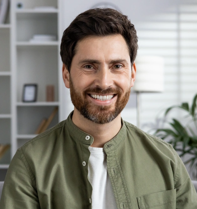 Smiling man with beard in dental office setting wearing olive button-up shirt.