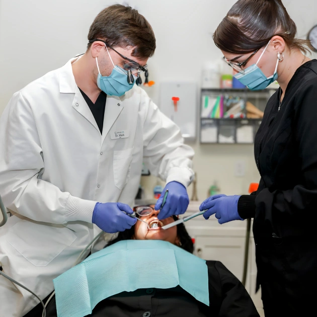 Dentist performing tooth extraction with assistant in Fitchburg dental office.